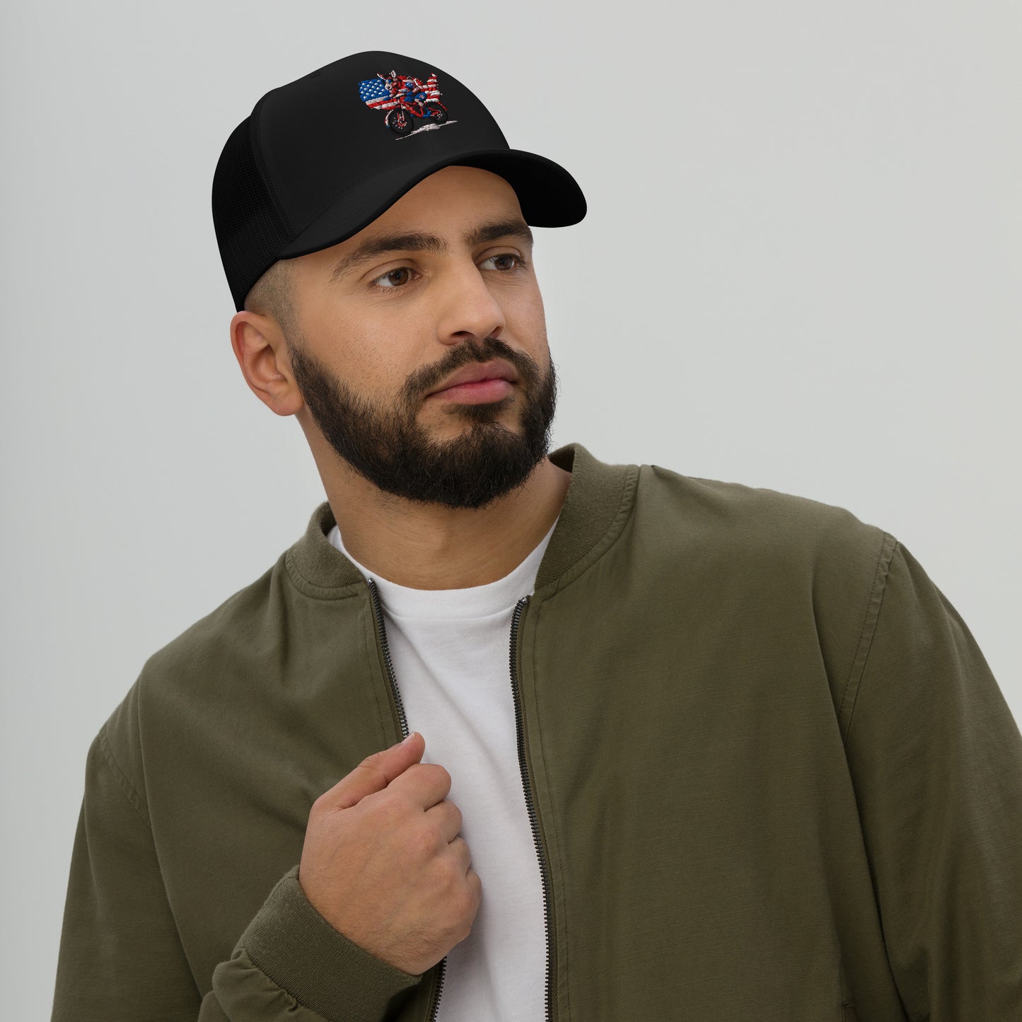 Man wearing a black cap with embroidery and an olive green jacket on a plain background
