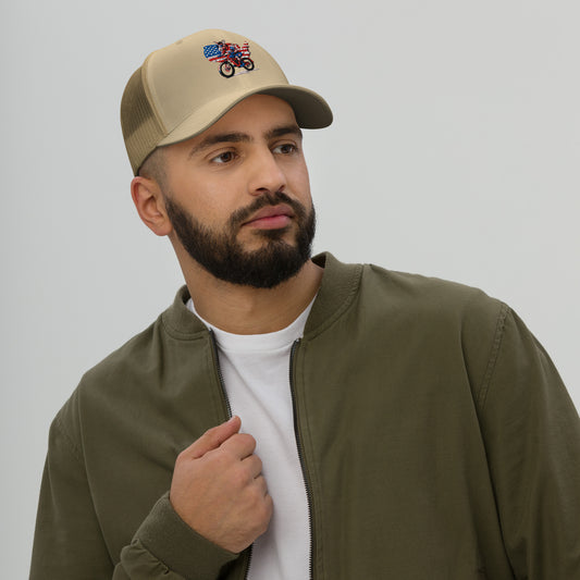 Man wearing a beige cap with an embroidered design and a green jacket over a white shirt.