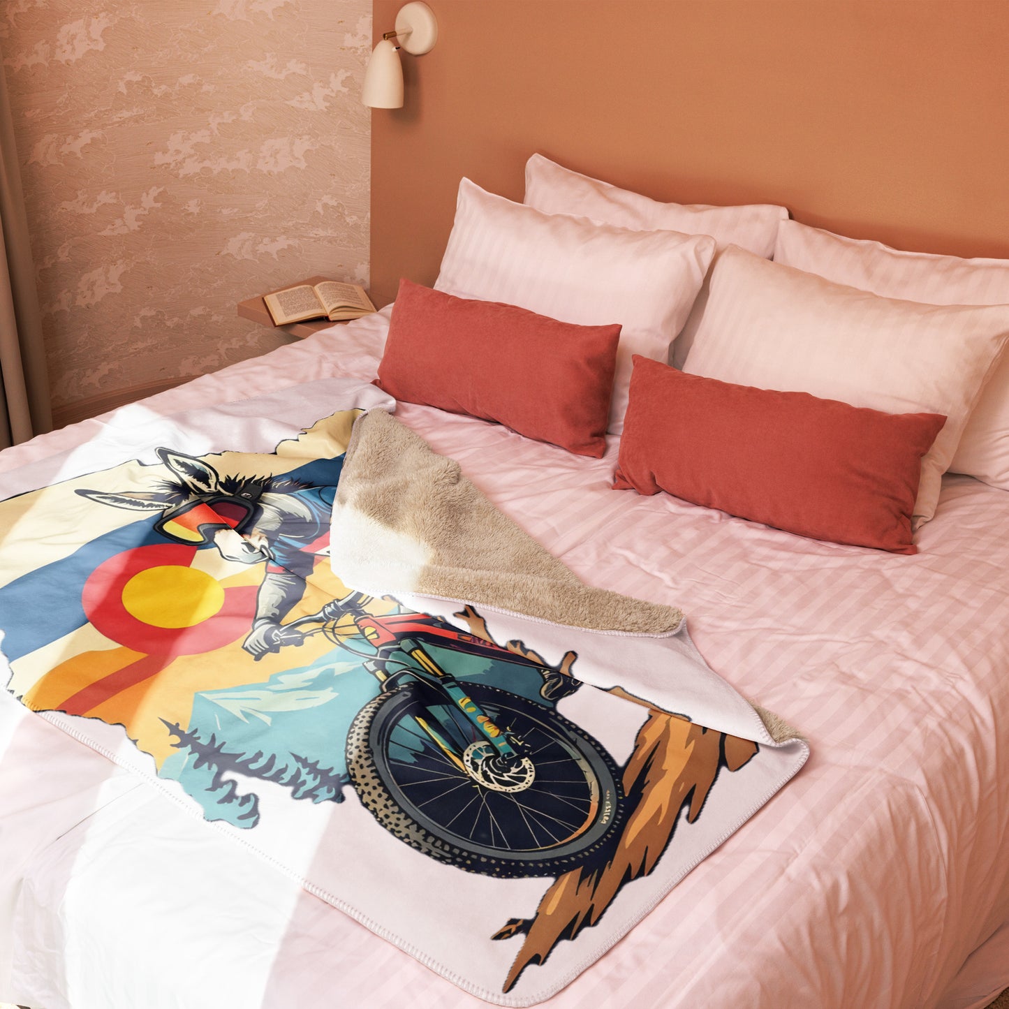 Colorful blanket with a bicycle and mountain design on a bed with red and white pillows.