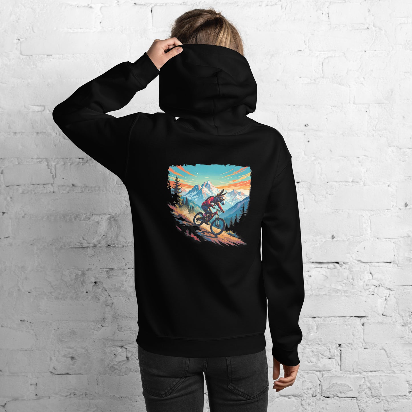 Person wearing a black hoodie with a mountain bike graphic on the back against a white brick wall.