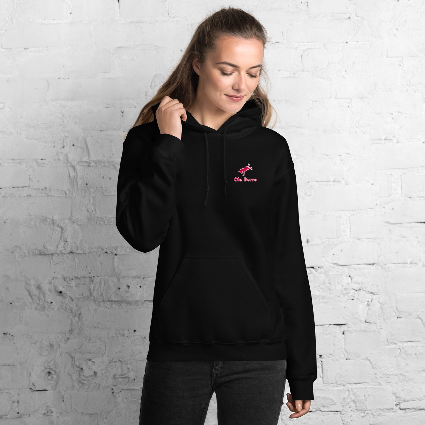 Person wearing a black hoodie with a logo against a white brick wall