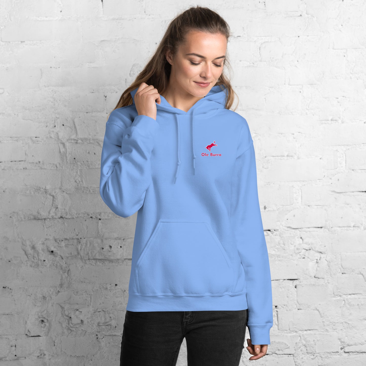 Woman wearing a light blue hoodie with a logo against a white brick wall