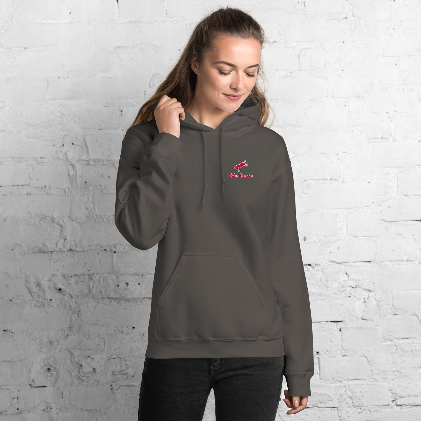 Person wearing a gray hoodie with a logo against a white brick wall