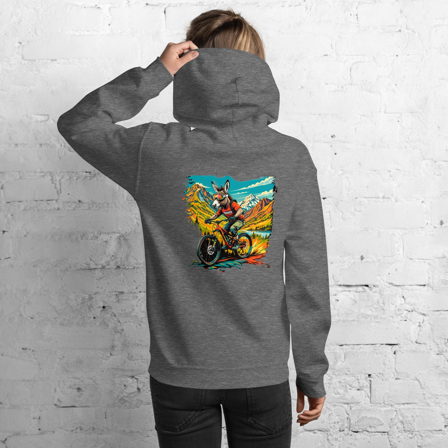 Person wearing a gray hoodie with a colorful graphic on the back against a white brick wall.