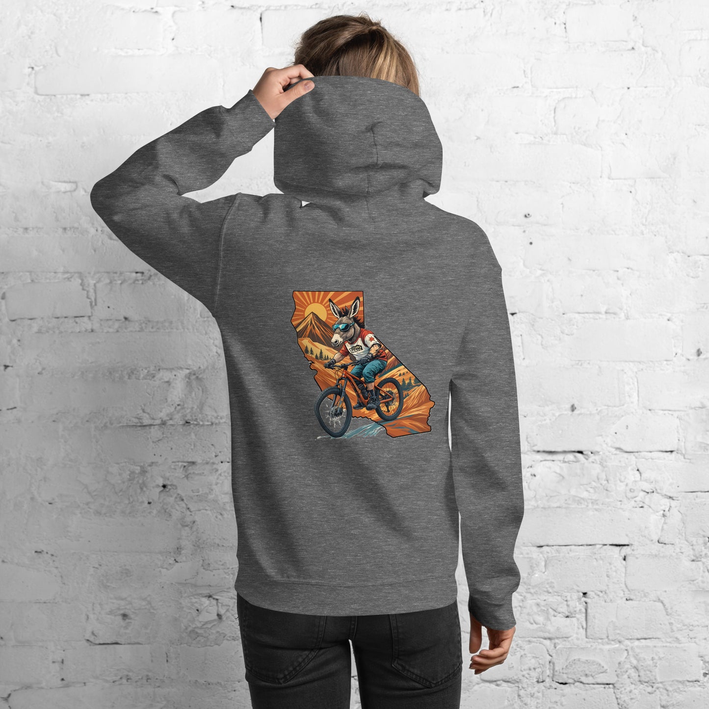 Person wearing a gray hoodie with a graphic of California on the back, standing against a white brick wall.