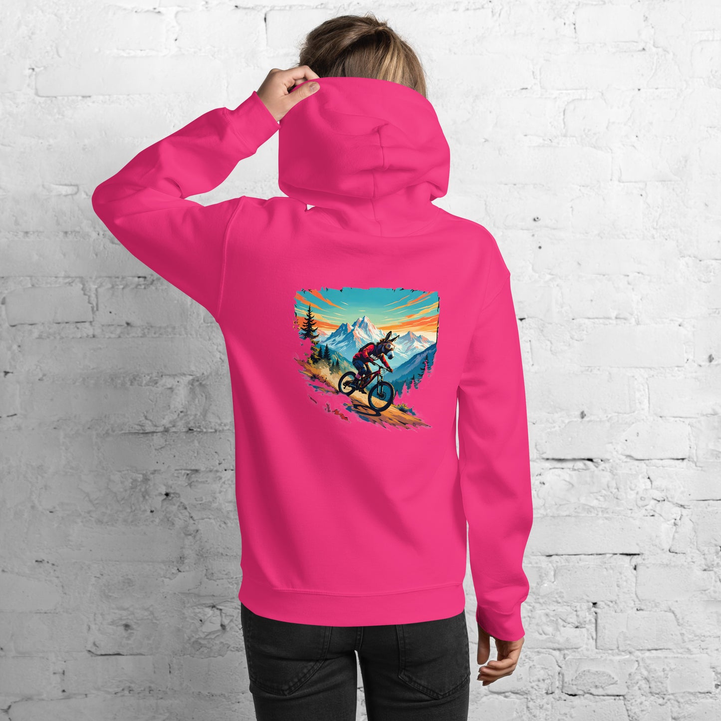 Person wearing a pink hoodie with a mountain bike design on the back against a white brick wall.