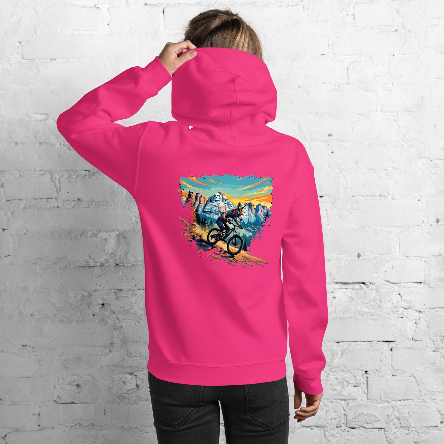 Person wearing a pink hoodie with a mountain bike design on the back against a white brick wall.