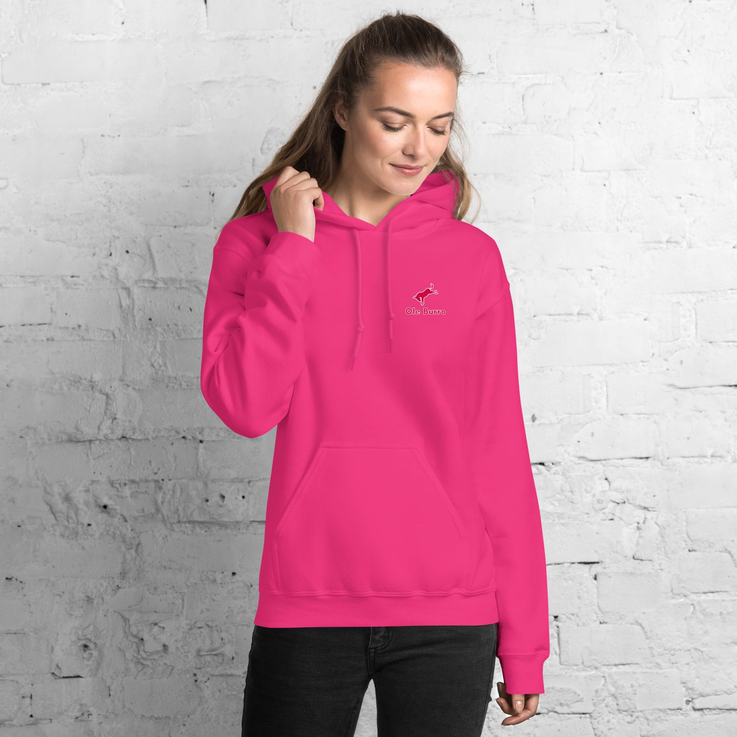 Person wearing a bright pink hoodie with a logo against a white brick wall.