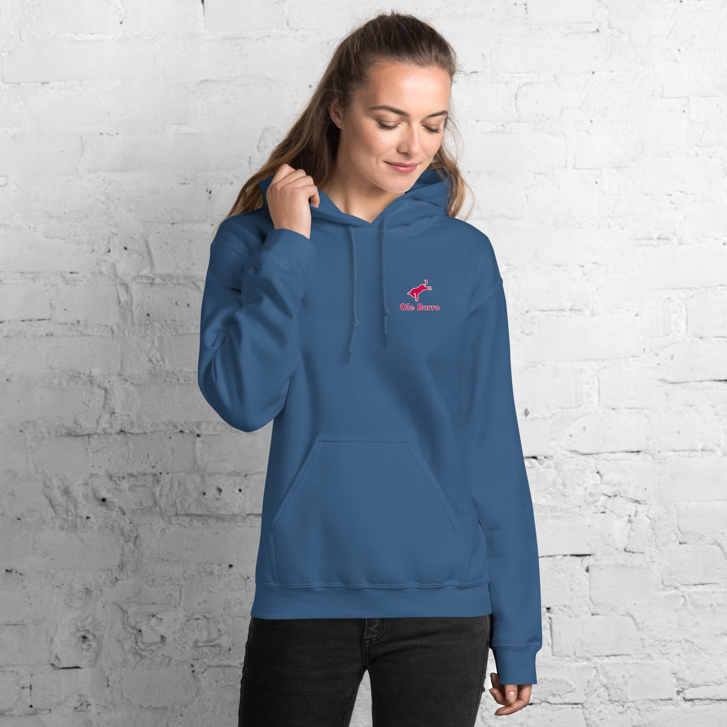 Person wearing a blue hoodie with a logo against a white brick wall