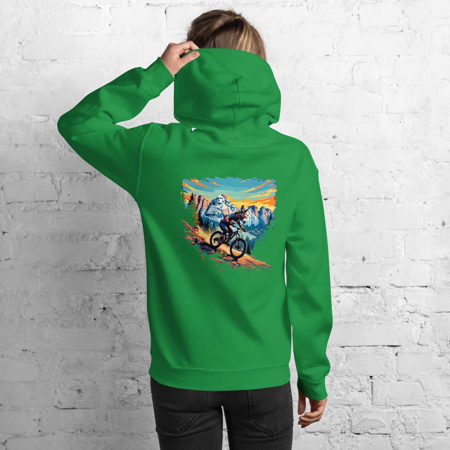 Person wearing a green hoodie with a mountain bike design on the back against a white brick wall.