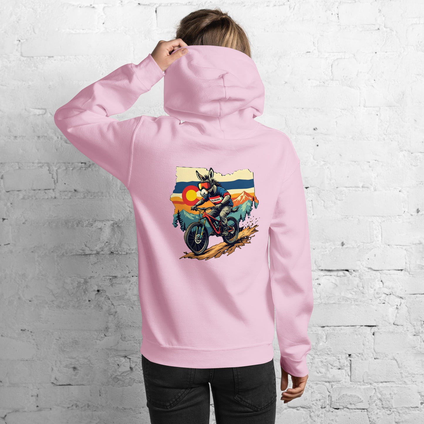 Person wearing a pink hoodie with a graphic design on the back against a white brick wall.