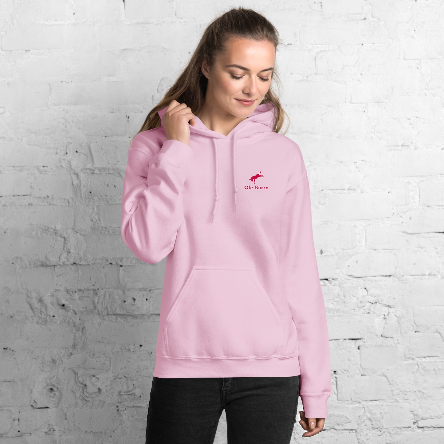 Woman wearing a pink hoodie with a logo against a white brick wall