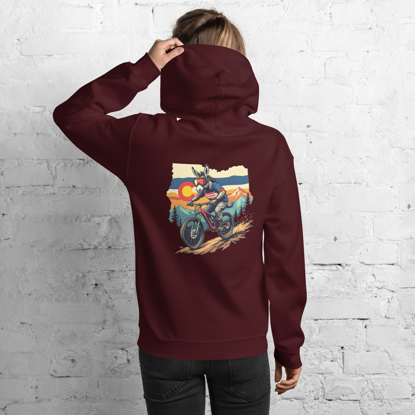 Person wearing a maroon hoodie with a graphic of a person on a motorcycle against a mountainous background.