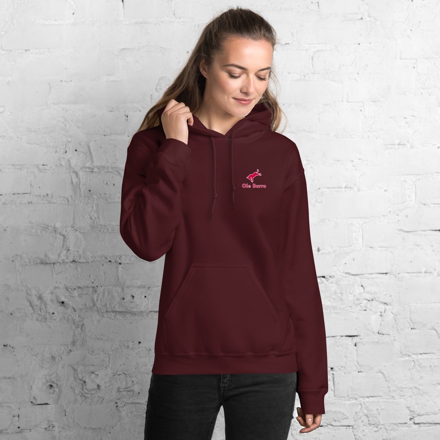 Person wearing a maroon hoodie with a logo against a white brick wall