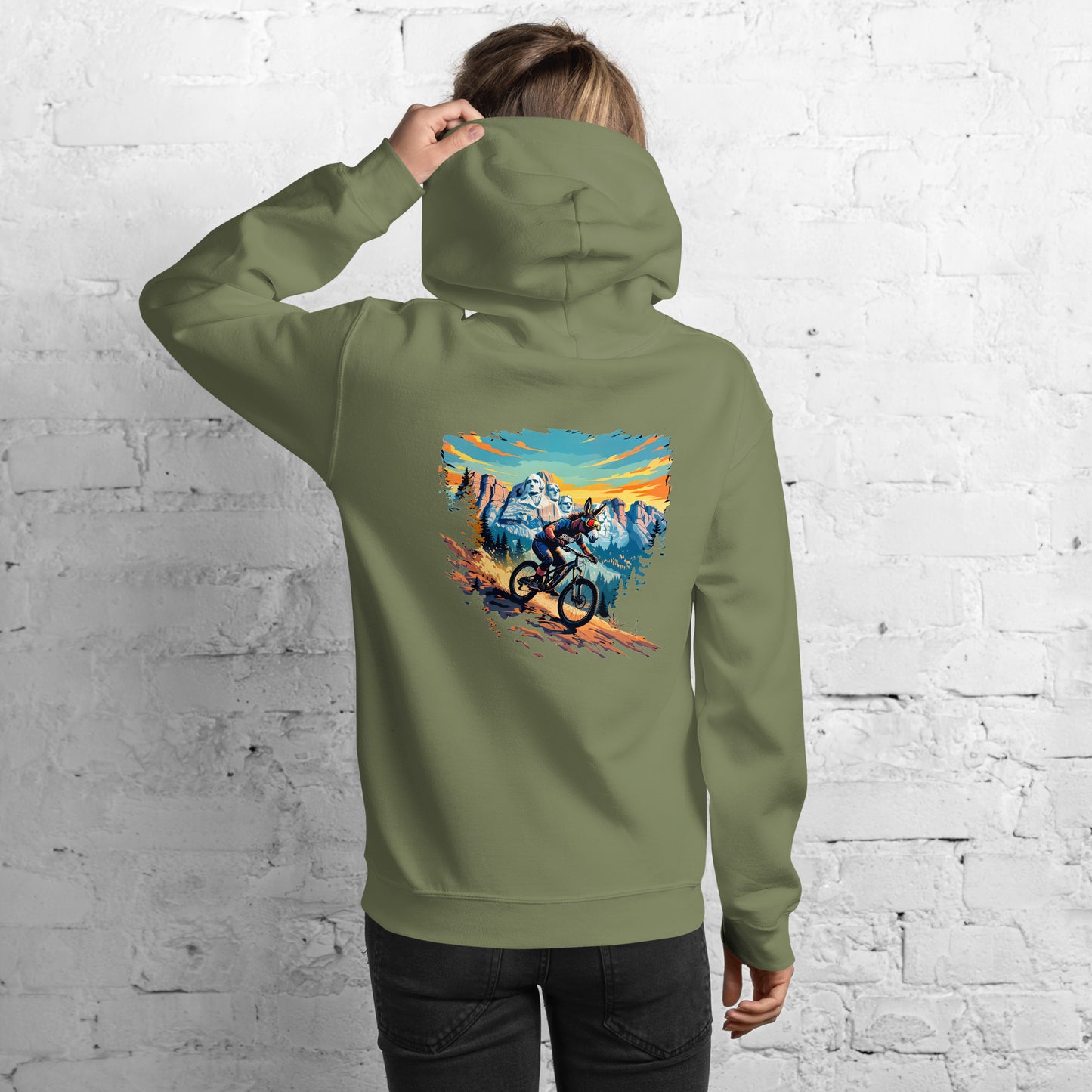 Person wearing a green hoodie with a mountain bike design on the back against a white brick wall.