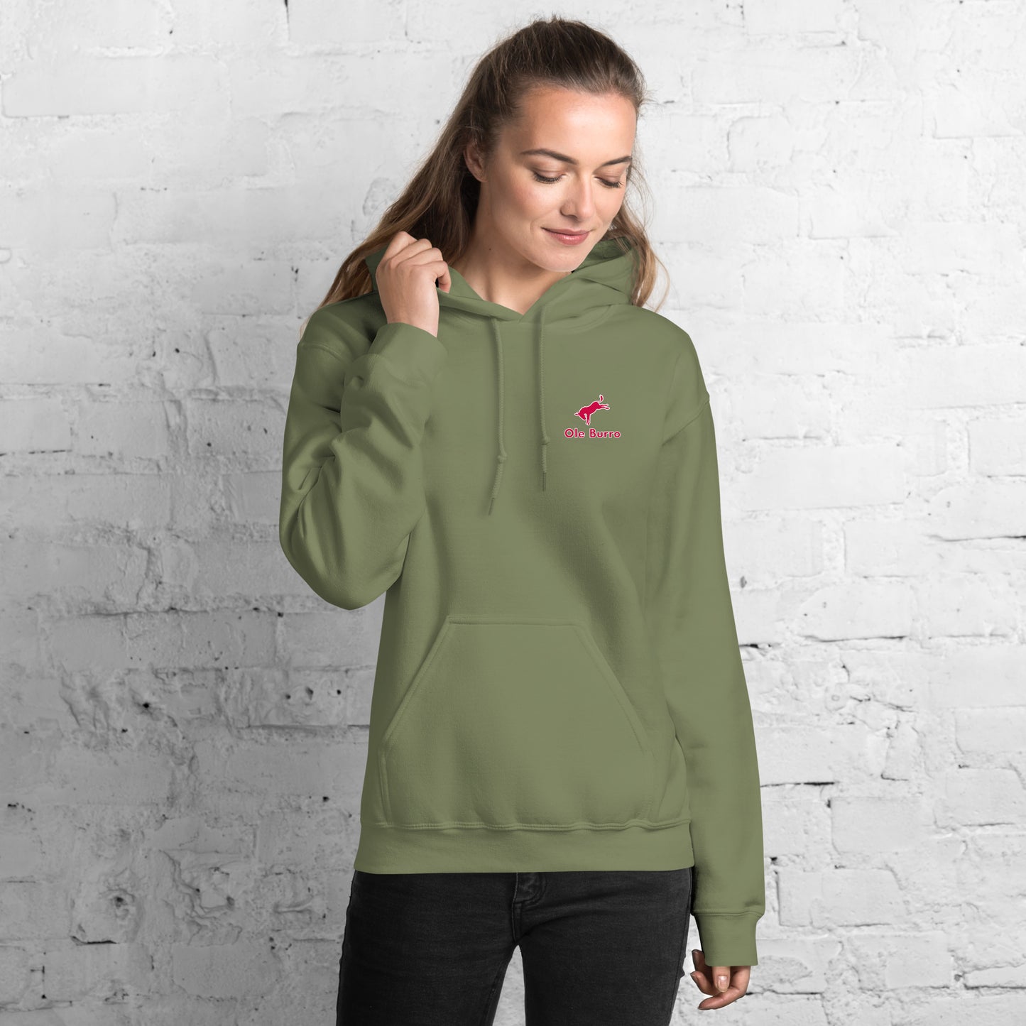 Person wearing a green hoodie with a logo against a white brick wall