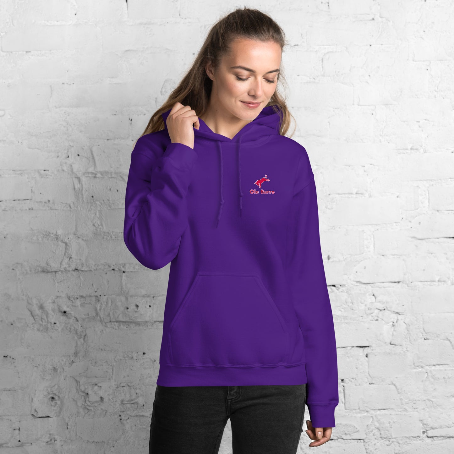 Person wearing a purple hoodie with a logo against a white brick wall