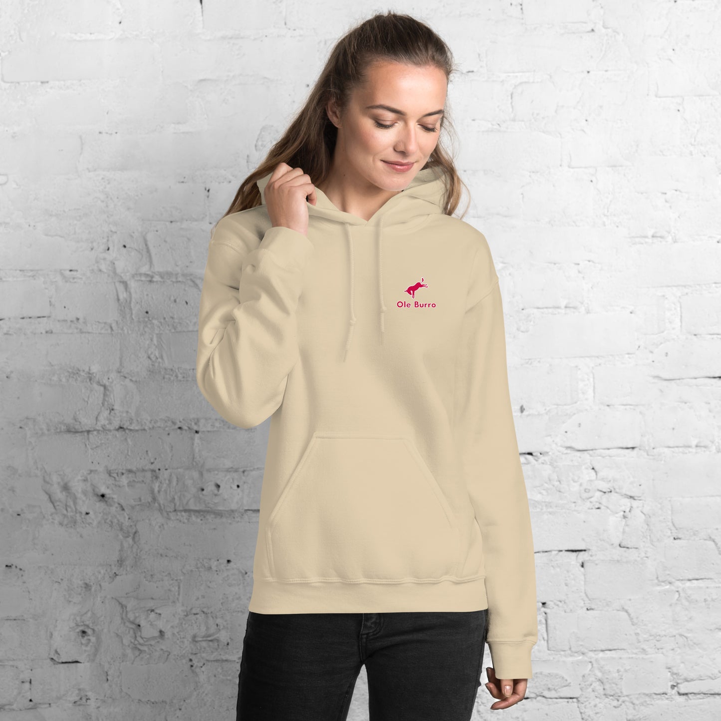 Woman wearing a beige hoodie with a red logo against a white brick wall
