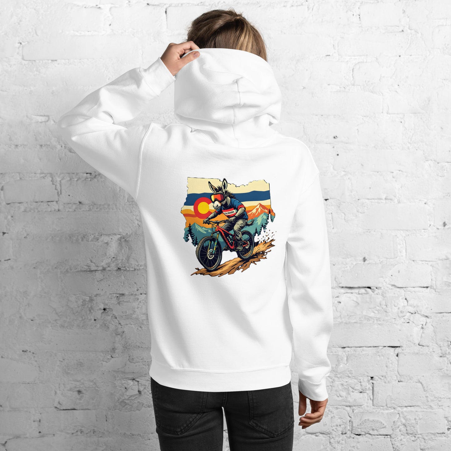 Person wearing a white hoodie with a colorful graphic of a motorcycle on the back, standing against a white brick wall.