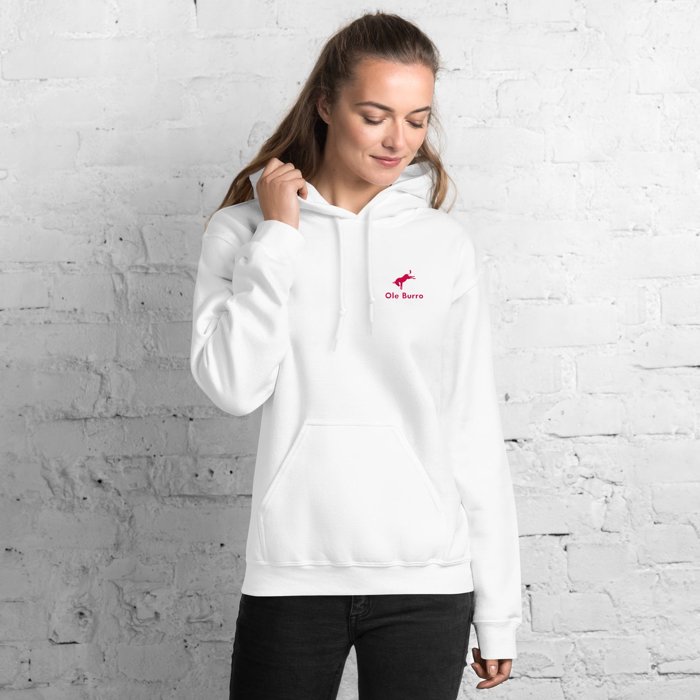 Woman wearing a white hoodie with a logo against a white brick wall