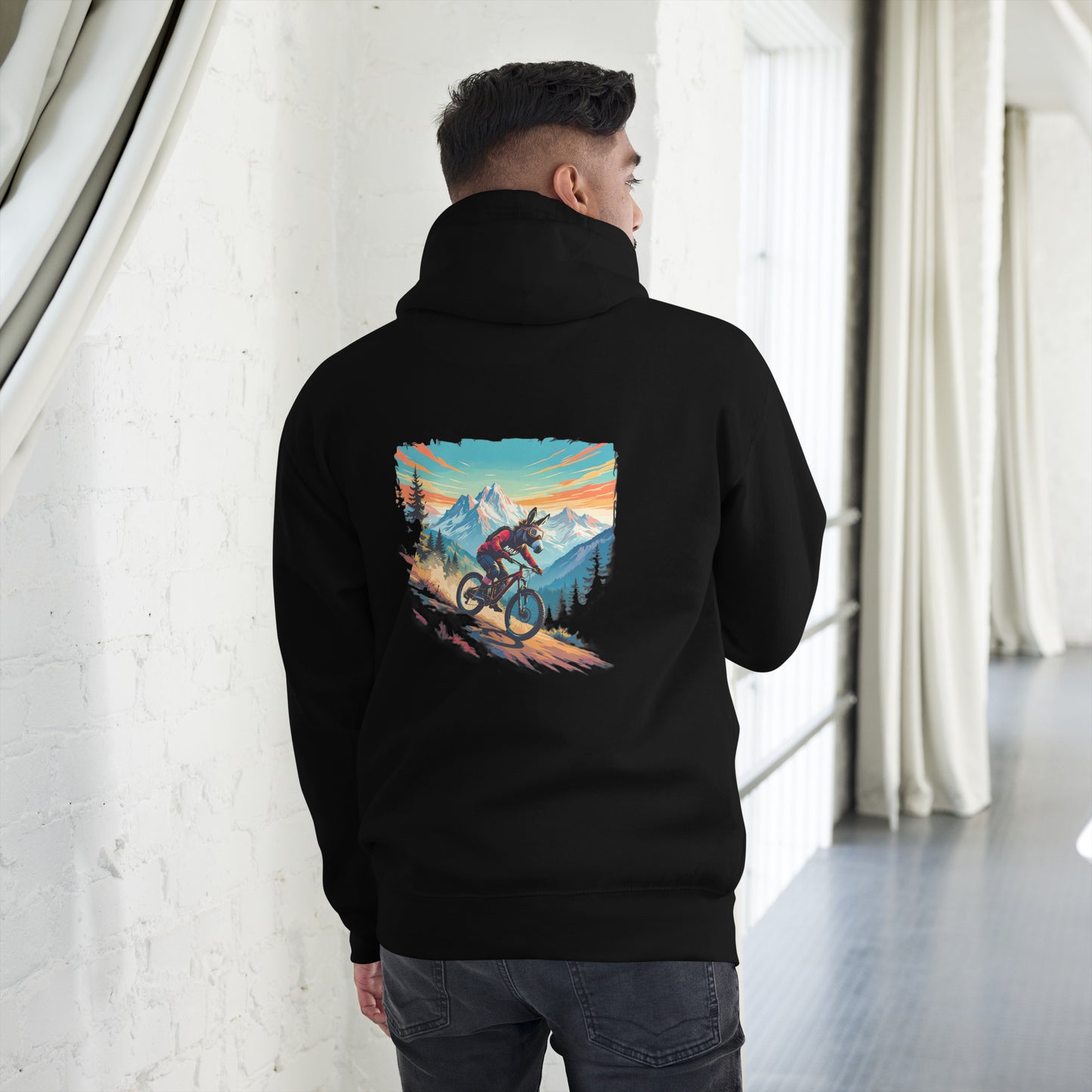 Person wearing a black hoodie with a mountain bike graphic on the back, standing in a room with white walls and curtains.