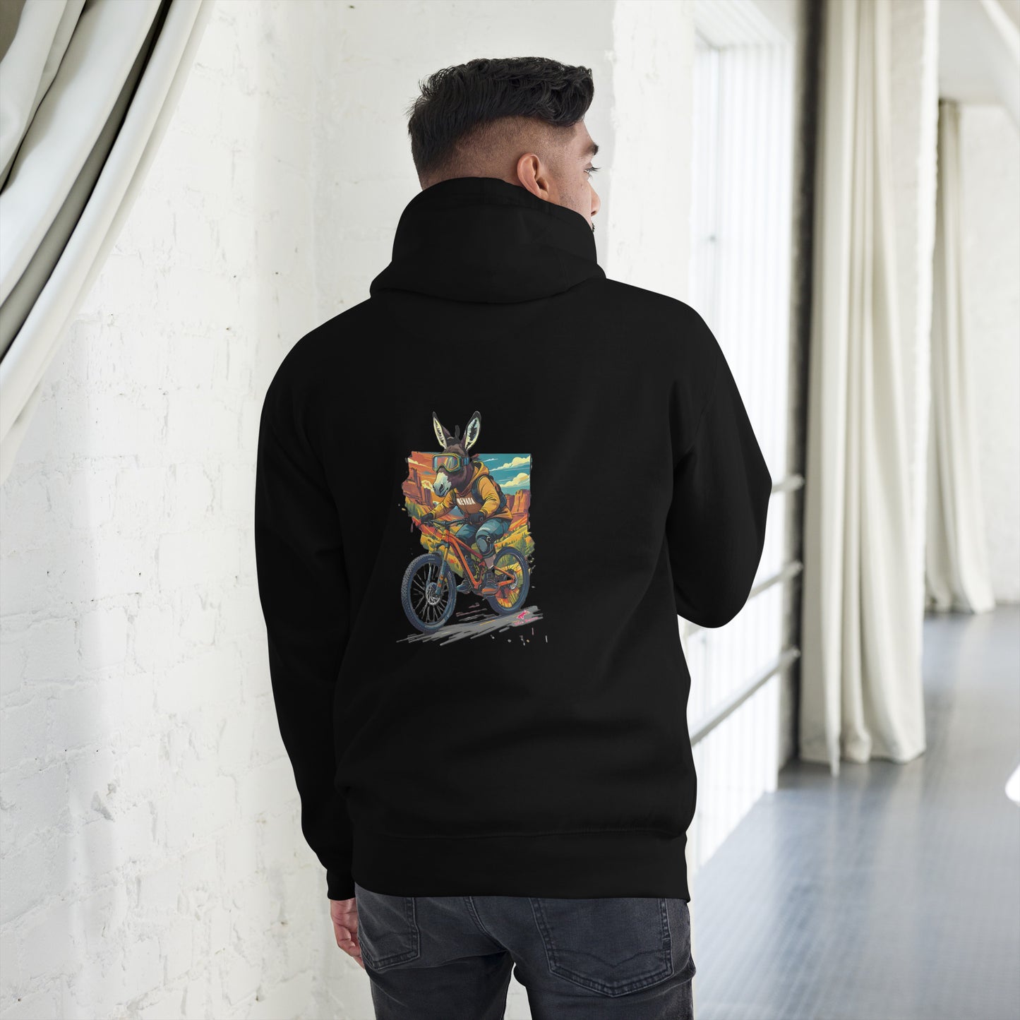 Person wearing a black hoodie with a colorful graphic on the back, standing in a room with white walls and curtains.