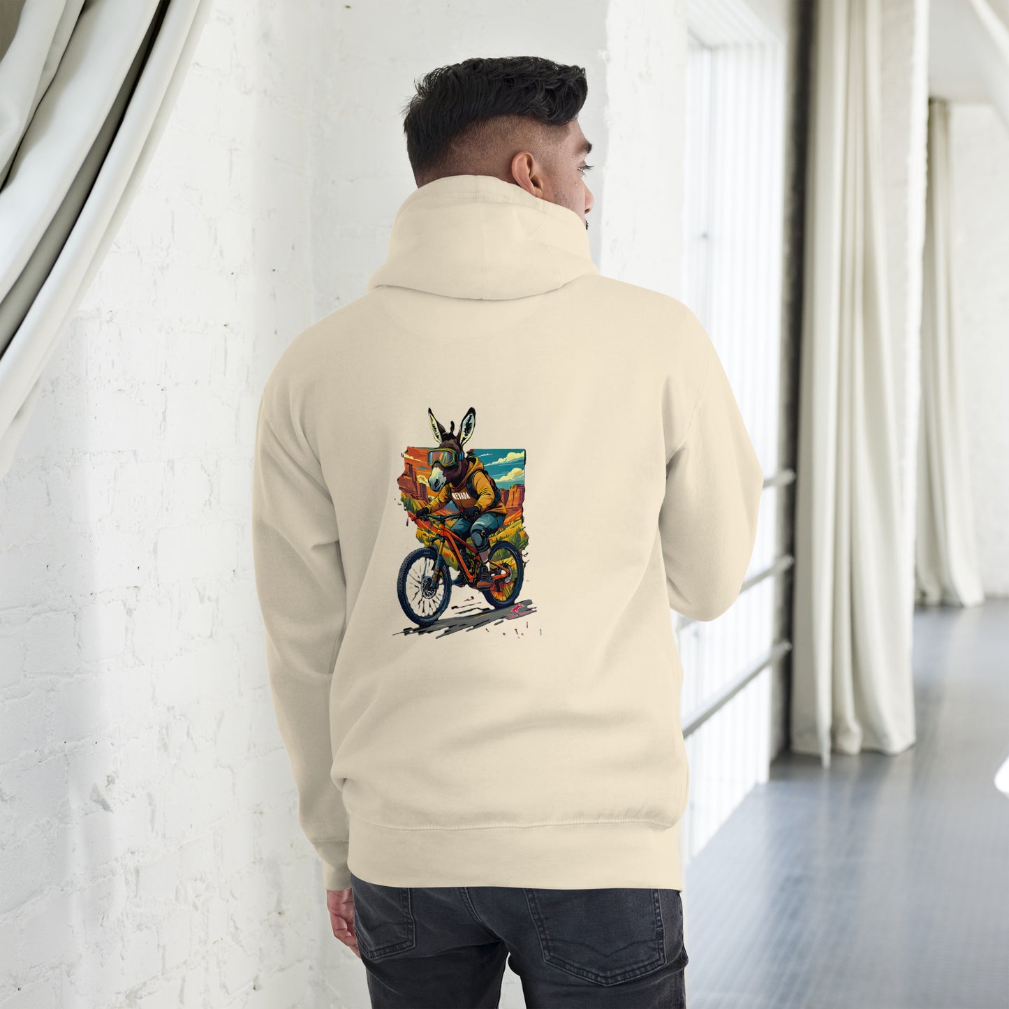 Person wearing a beige hoodie with a colorful graphic on the back, standing in a room with white walls and a window.