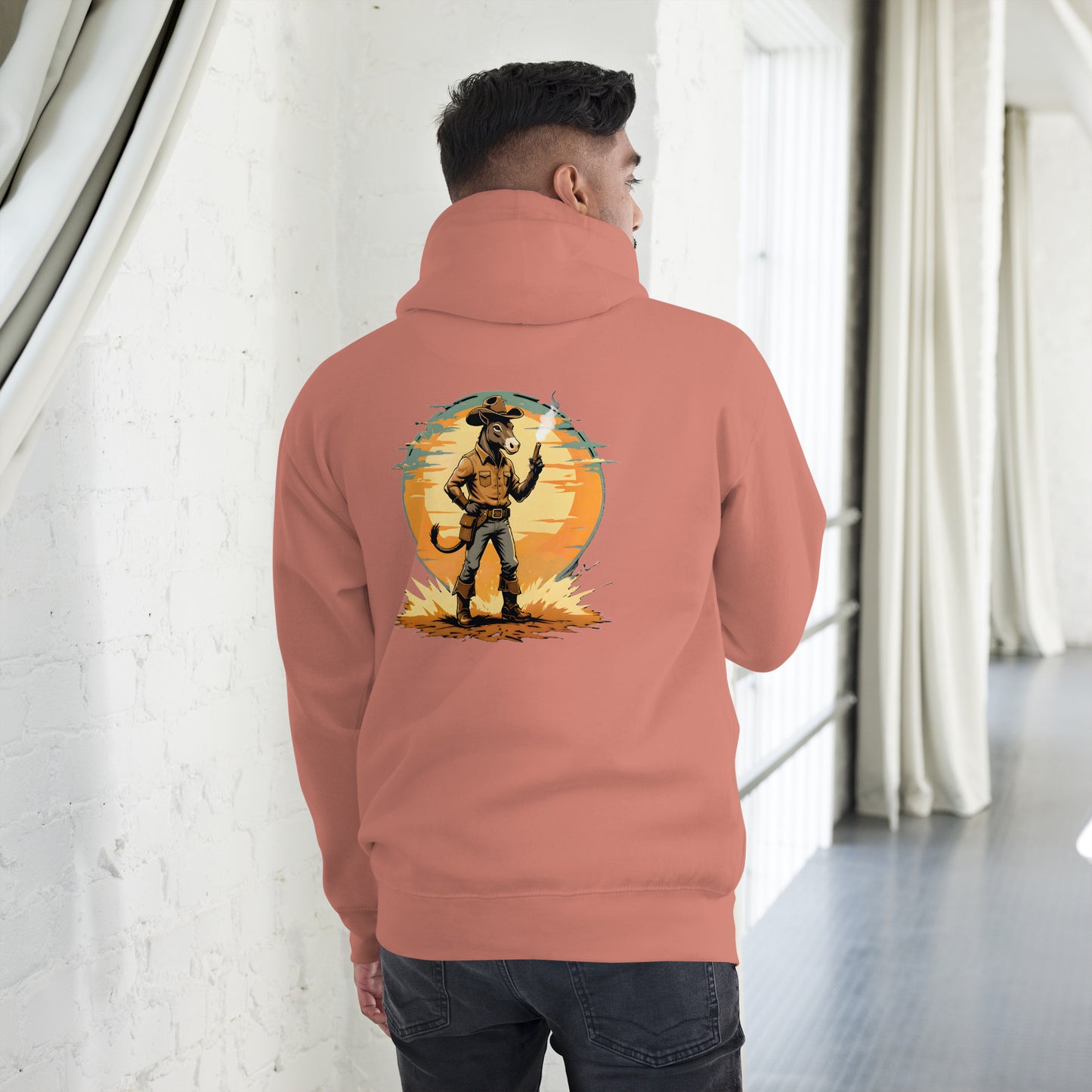 Person wearing a peach hoodie with a graphic design on the back, standing in a room with white walls and a gray floor.