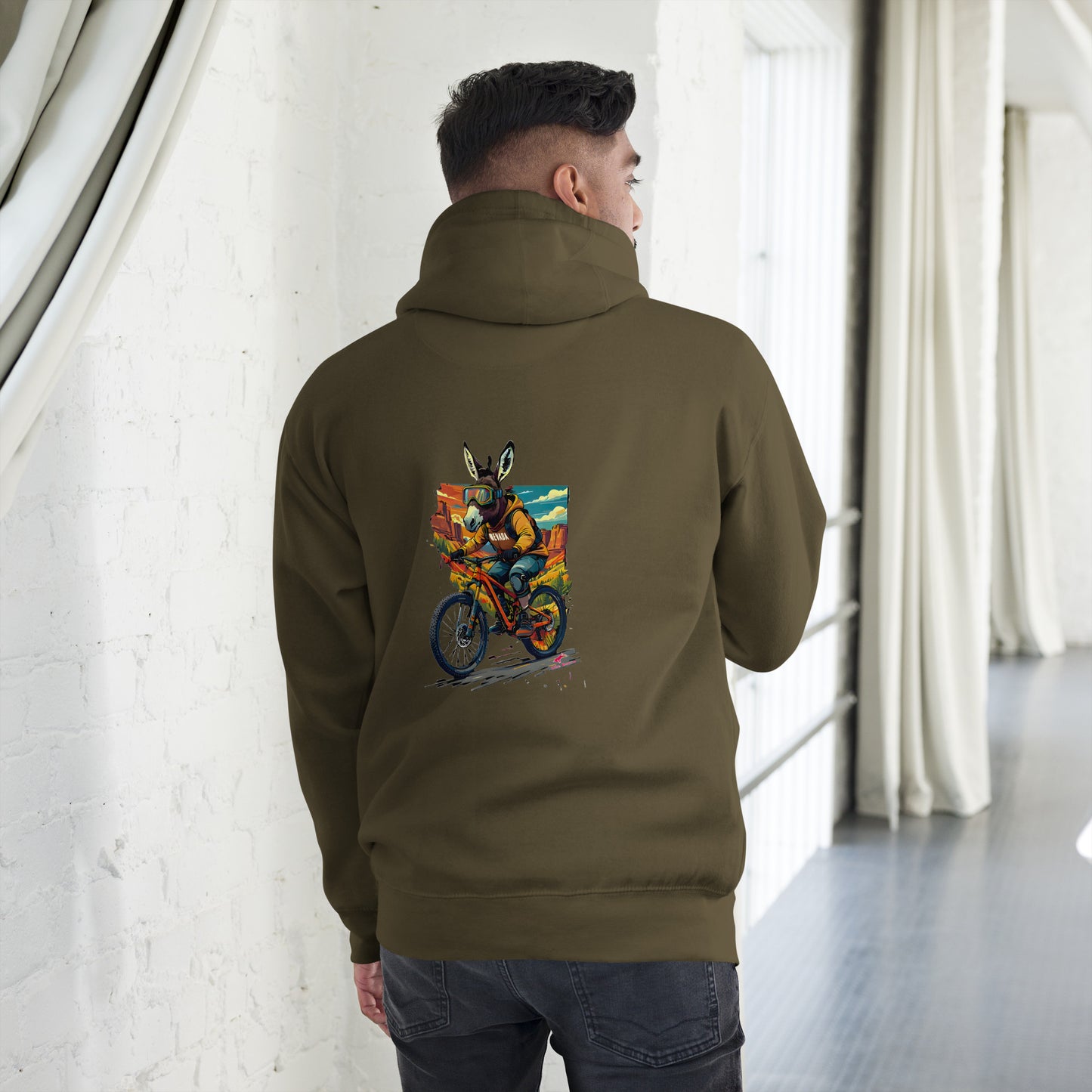 Person wearing a green hoodie with a colorful graphic on the back, standing in a room with white walls and curtains.