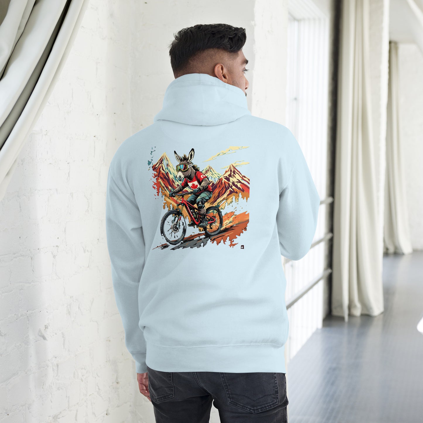 Person wearing a light blue hoodie with a colorful graphic on the back, standing in a room with white walls and a gray floor.