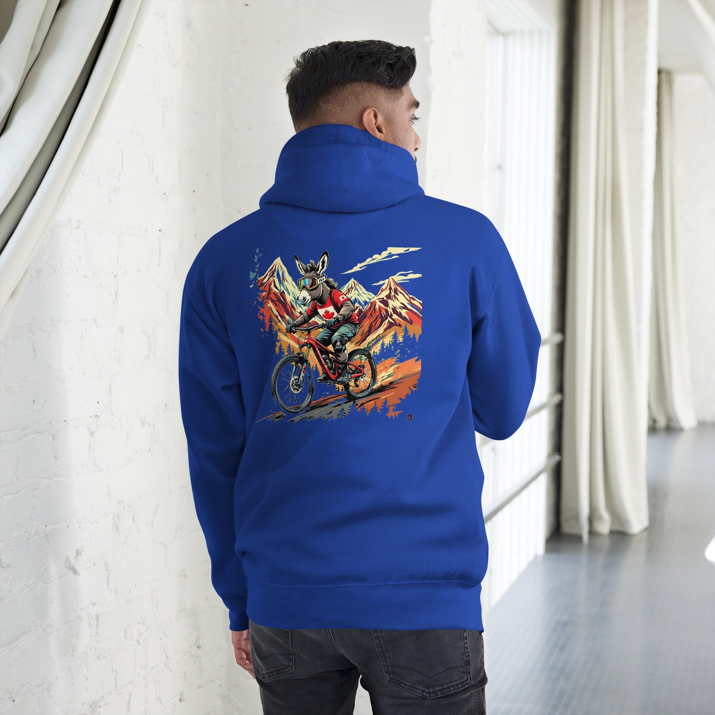 Person wearing a blue hoodie with a colorful graphic on the back, standing in a room with white walls and gray floor.