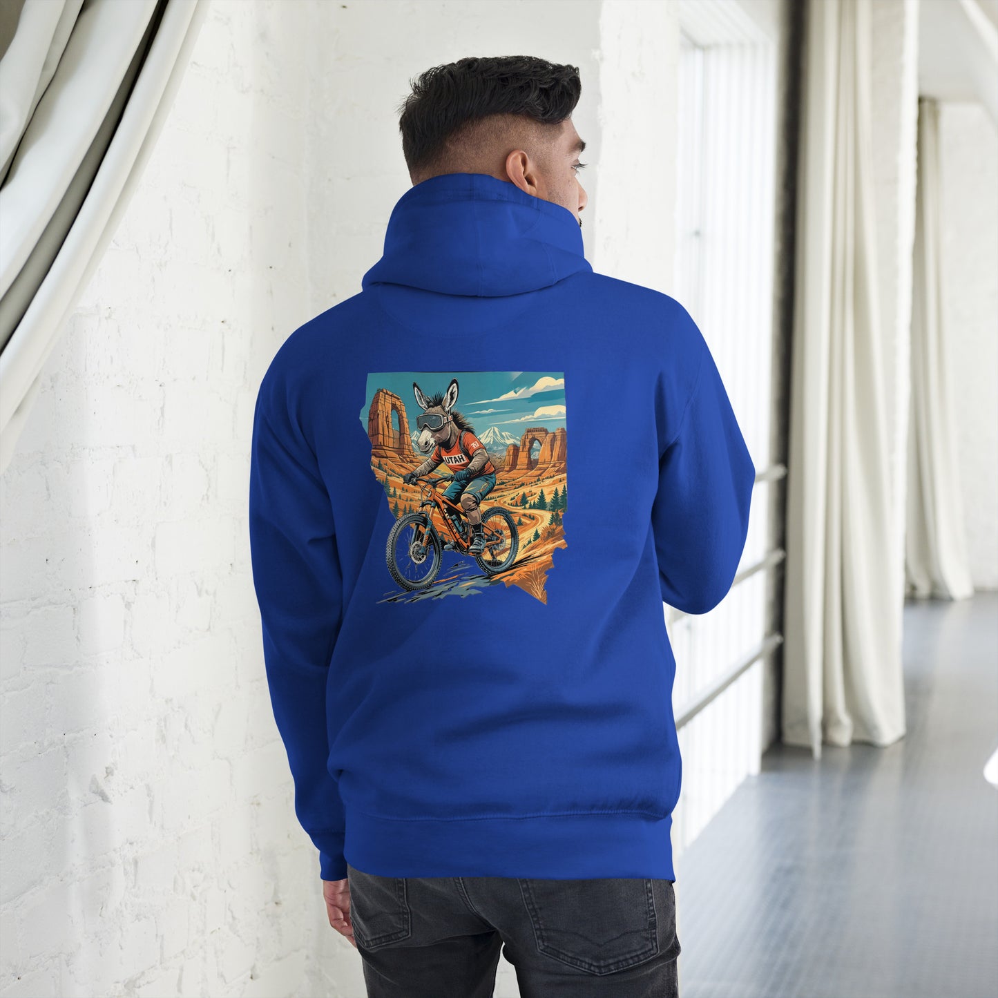 Person wearing a blue hoodie with a colorful graphic on the back, standing in a room with white walls and gray floor.