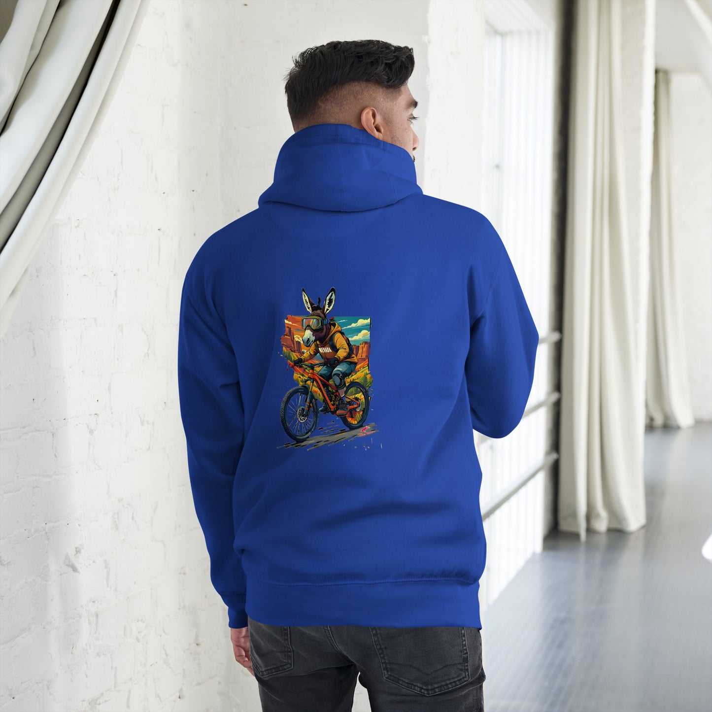 Person wearing a blue hoodie with a colorful graphic on the back, standing in a room with white walls and gray floor.