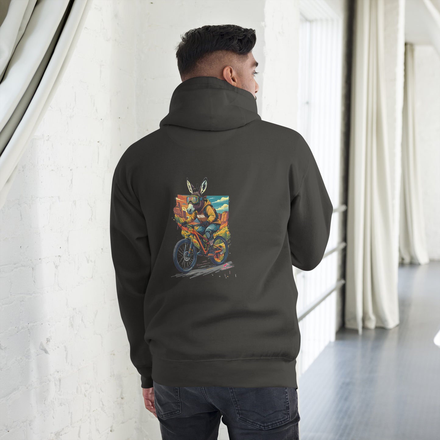 Person wearing a black hoodie with a colorful graphic on the back, standing in a room with white walls and curtains.