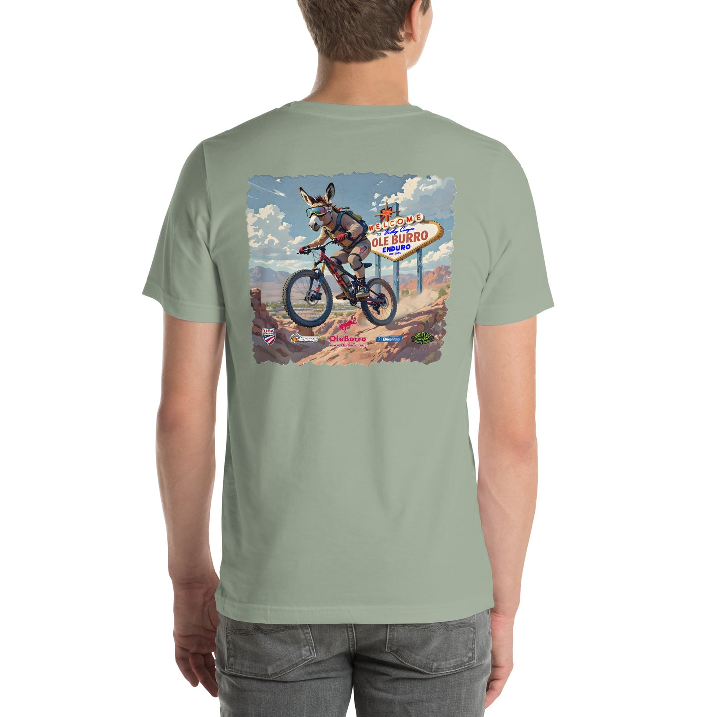 Person wearing a light green t-shirt with a graphic of a burro on a mountain bike on the back. and a sign in the desert.