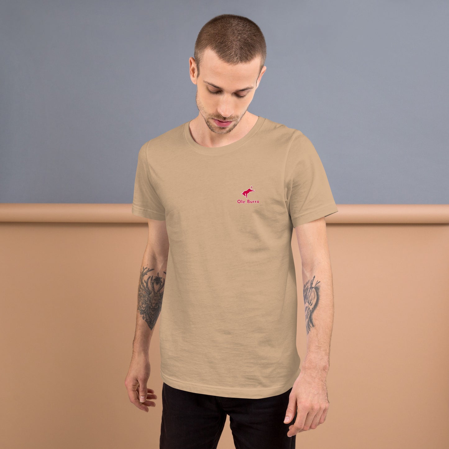 Man wearing a beige t-shirt with a small logo on a plain background
