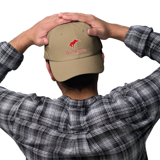 Person wearing a beige cap with 'Ole Burro' logo, holding it on their head against a white background