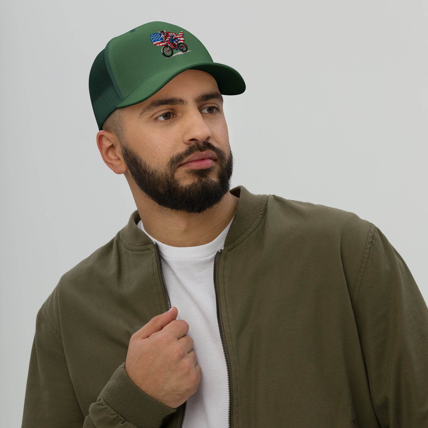 Man wearing a green cap with an embroidered design and a green jacket on a plain background