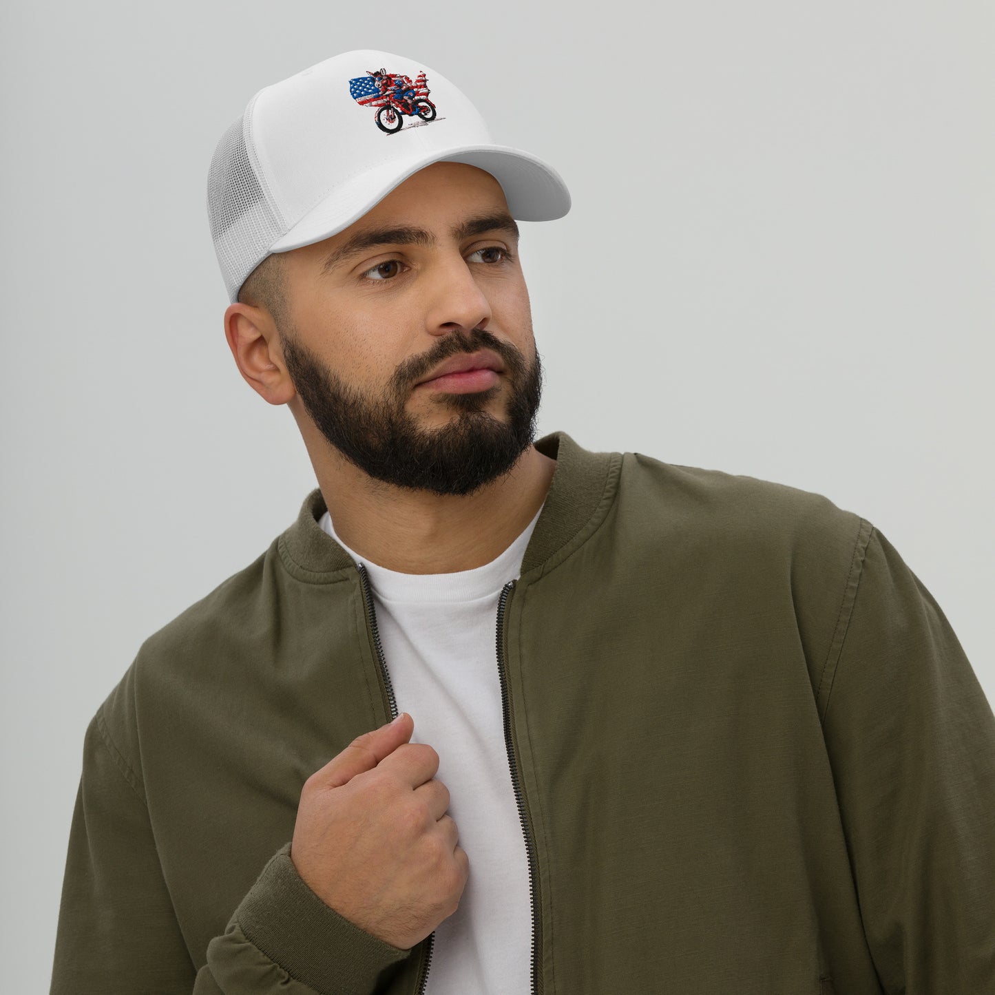 Man wearing a white cap with a design, olive green jacket, and white shirt on a gray background