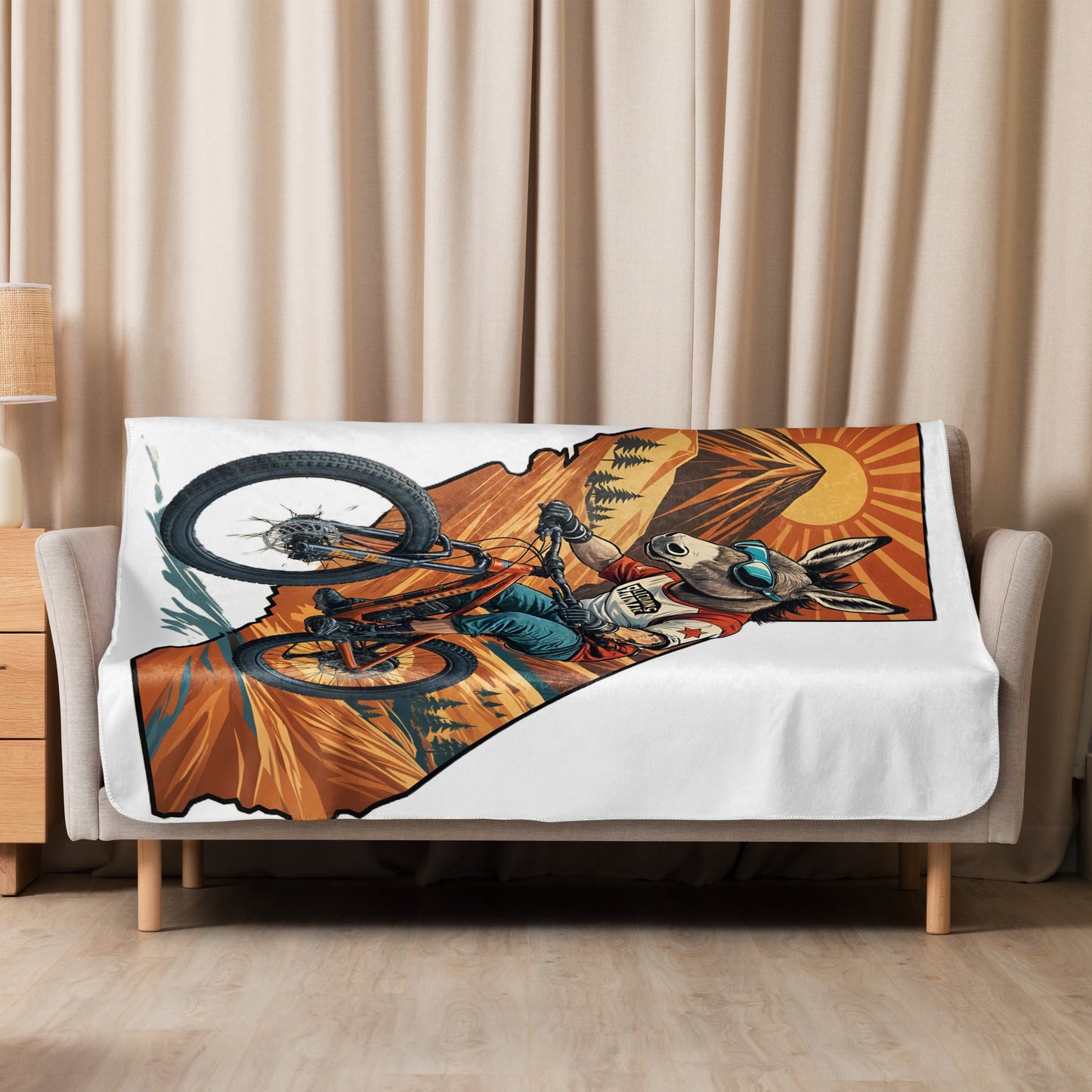 Blanket with a mountain biking design draped over a bed in a room with beige curtains.