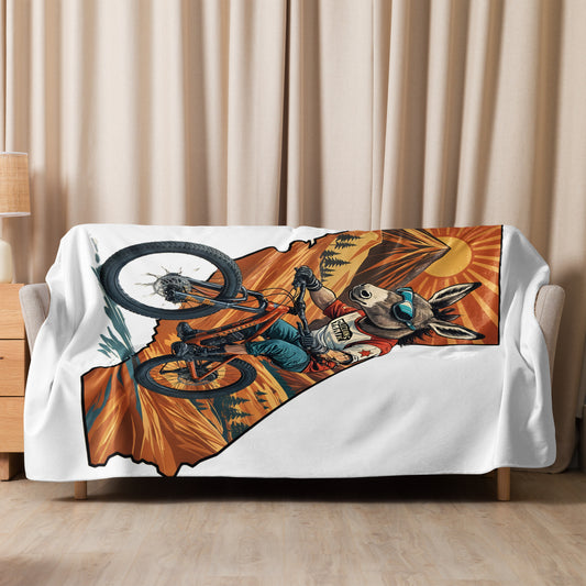 Sofa with a blanket featuring a mountain biker design draped over it, against a beige curtain background.