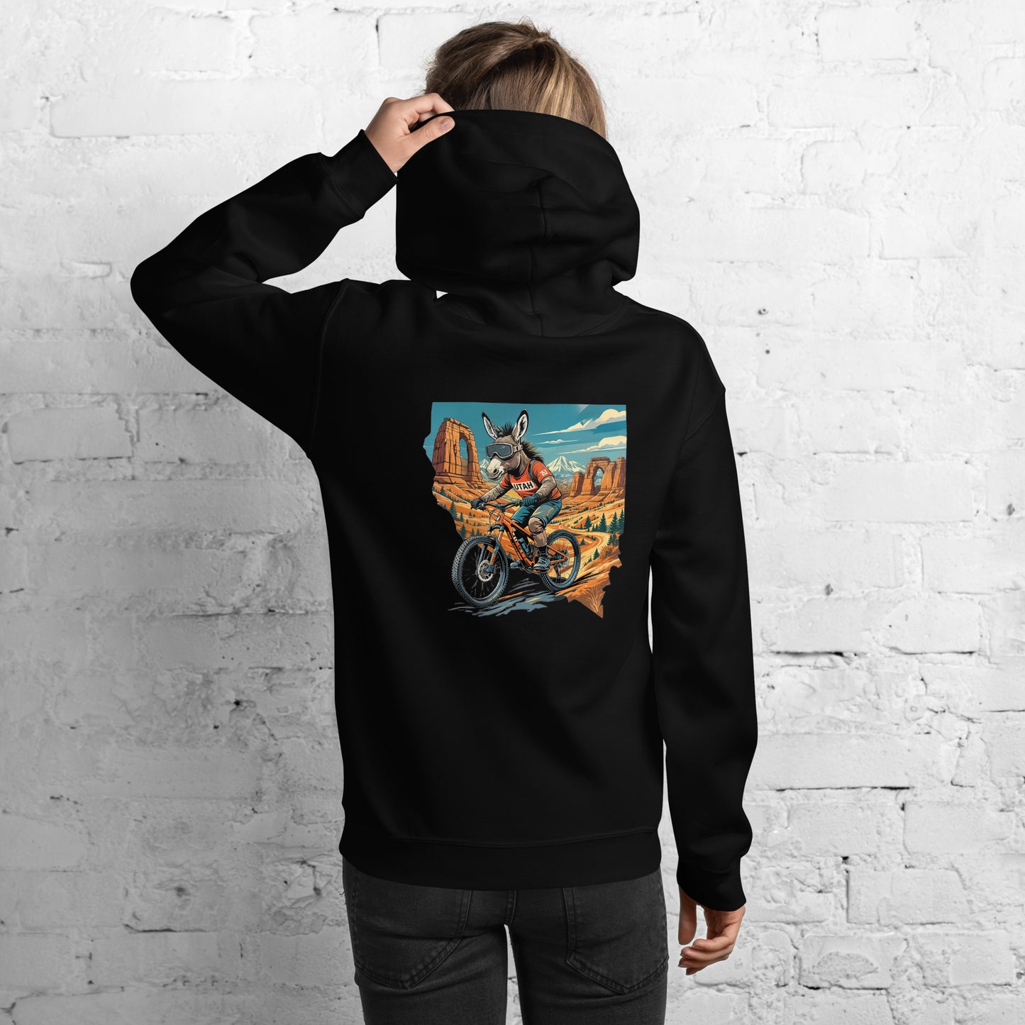 Person wearing a black hoodie with a colorful graphic on the back against a white brick wall.