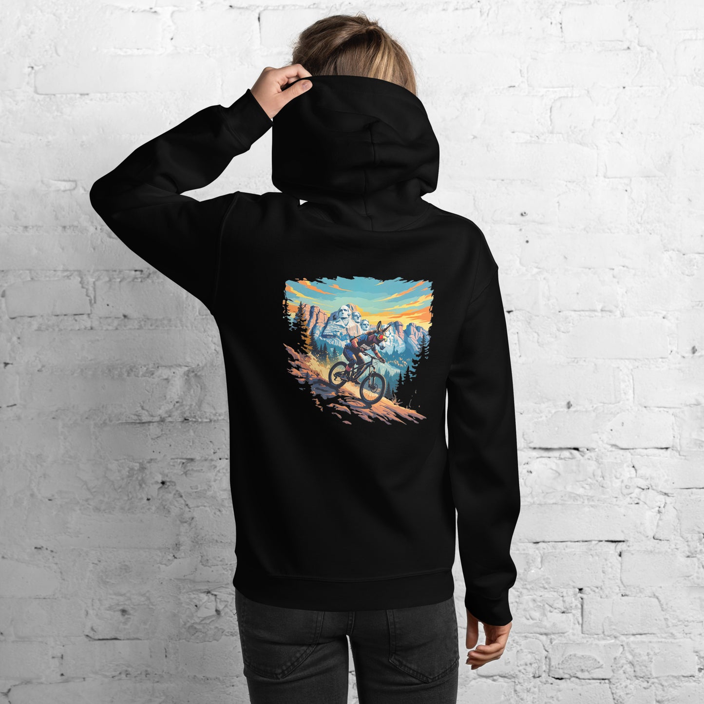 Person wearing a black hoodie with a mountain bike graphic on the back against a white brick wall.