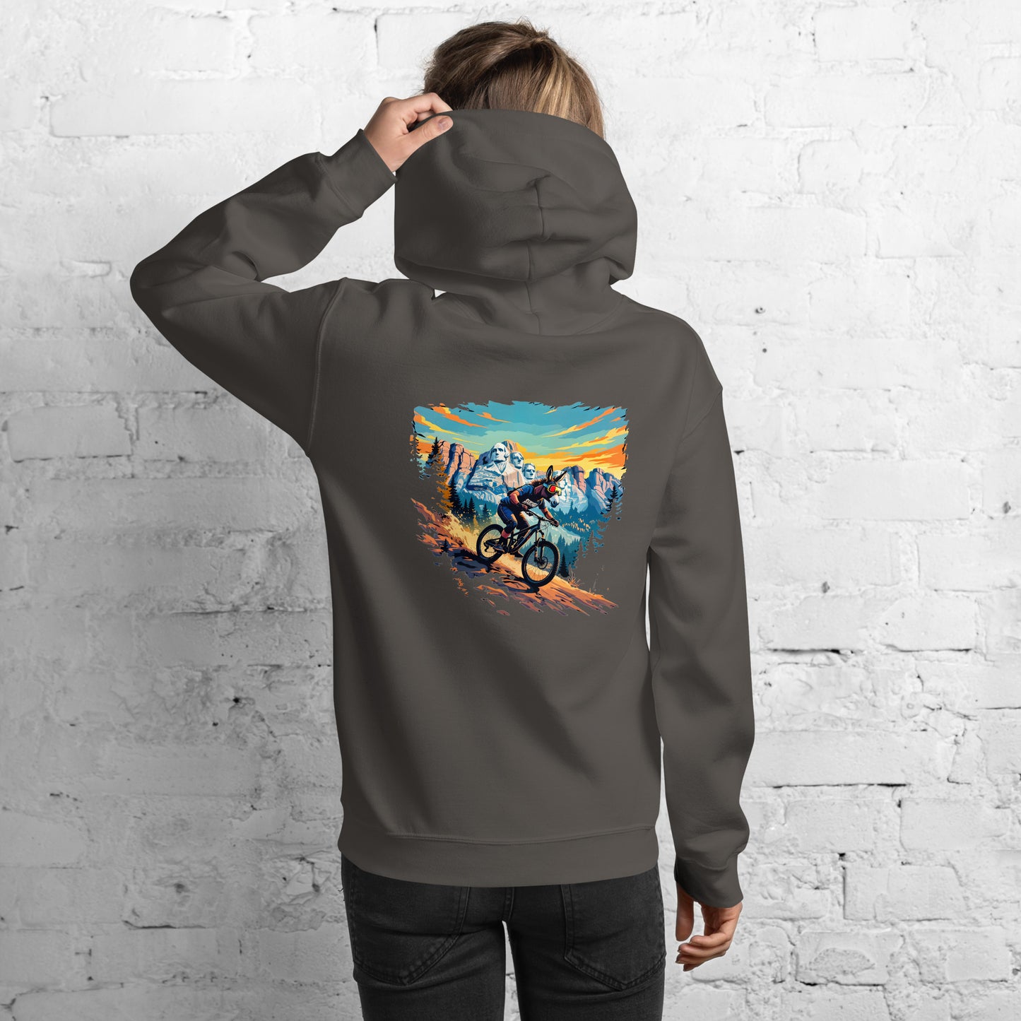 Person wearing a gray hoodie with a mountain bike design on the back against a white brick wall.