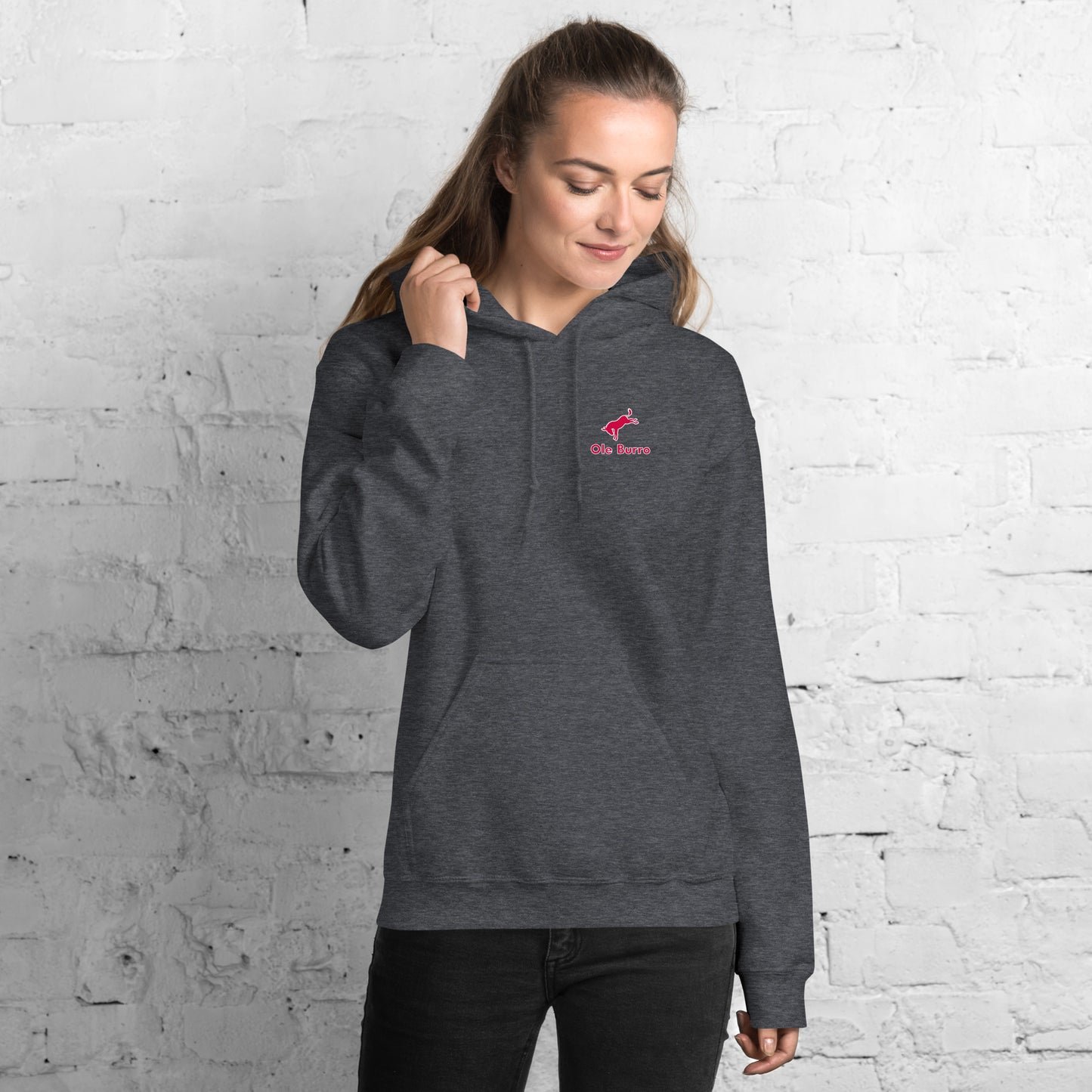 Woman wearing a gray hoodie with a pink logo against a white brick wall