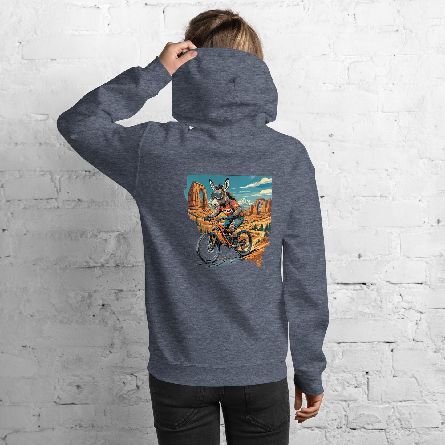 Person wearing a gray hoodie with a colorful graphic on the back against a white brick wall.