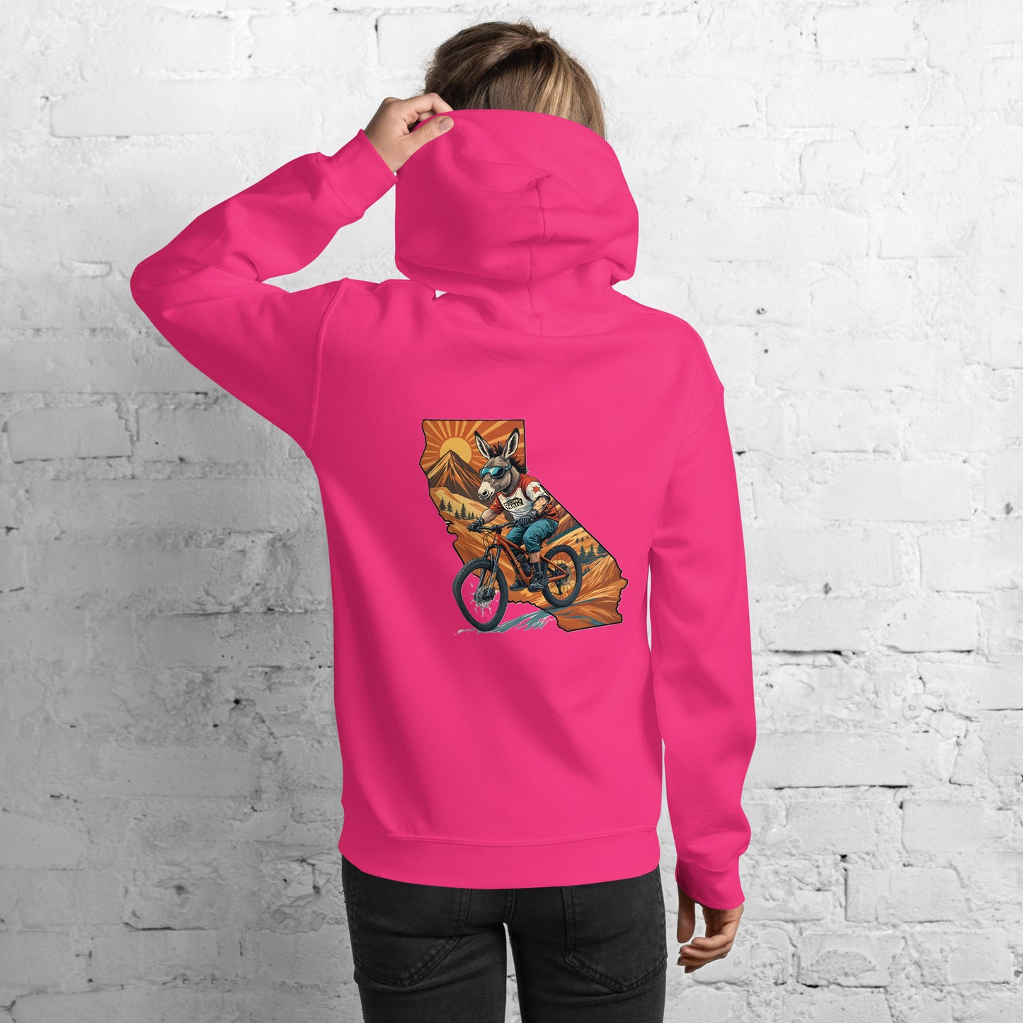 Person wearing a pink hoodie with a graphic of California on the back, standing against a white brick wall.