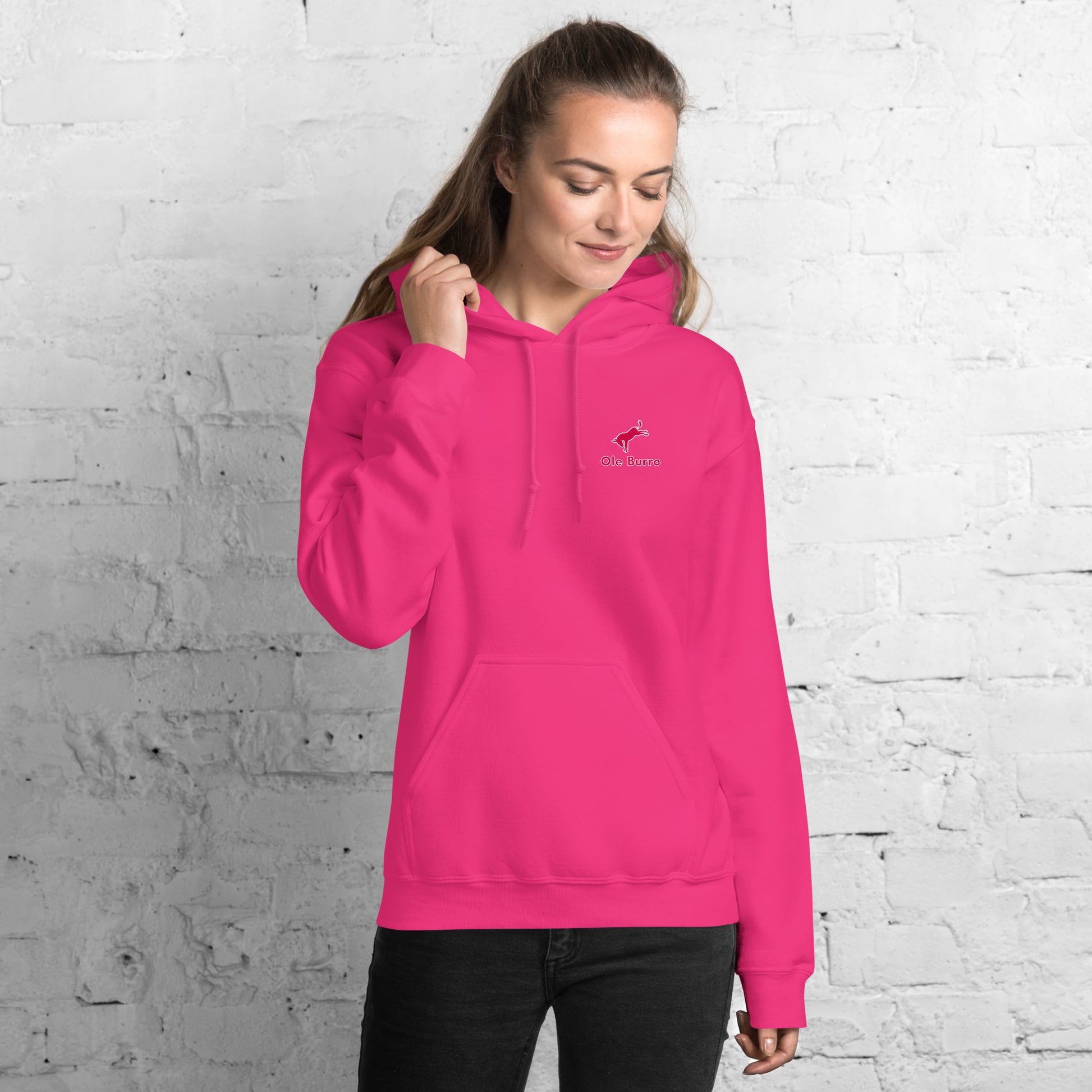 Person wearing a bright pink hoodie with a logo against a white brick wall.
