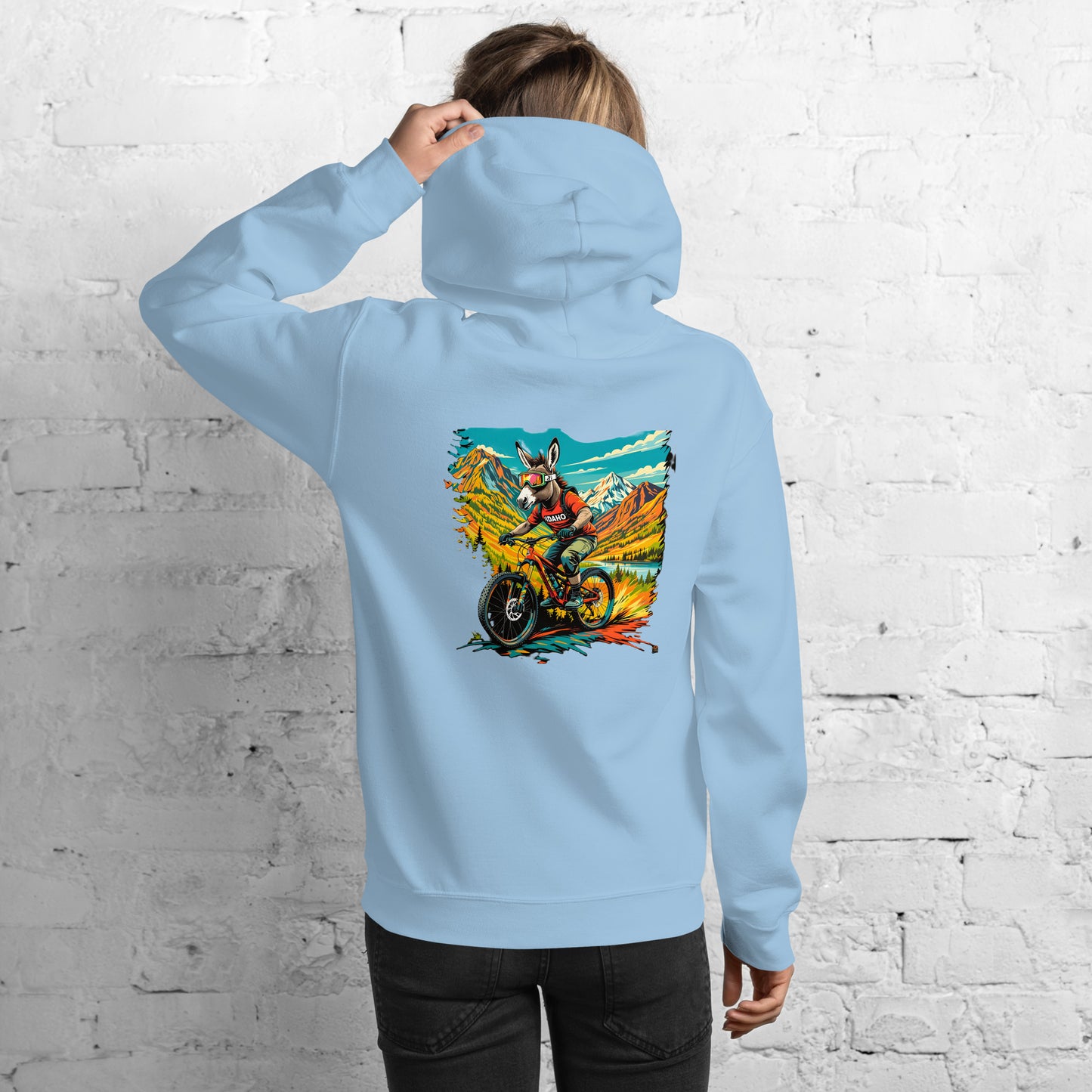 Person wearing a light blue hoodie with a colorful graphic on the back against a white brick wall.