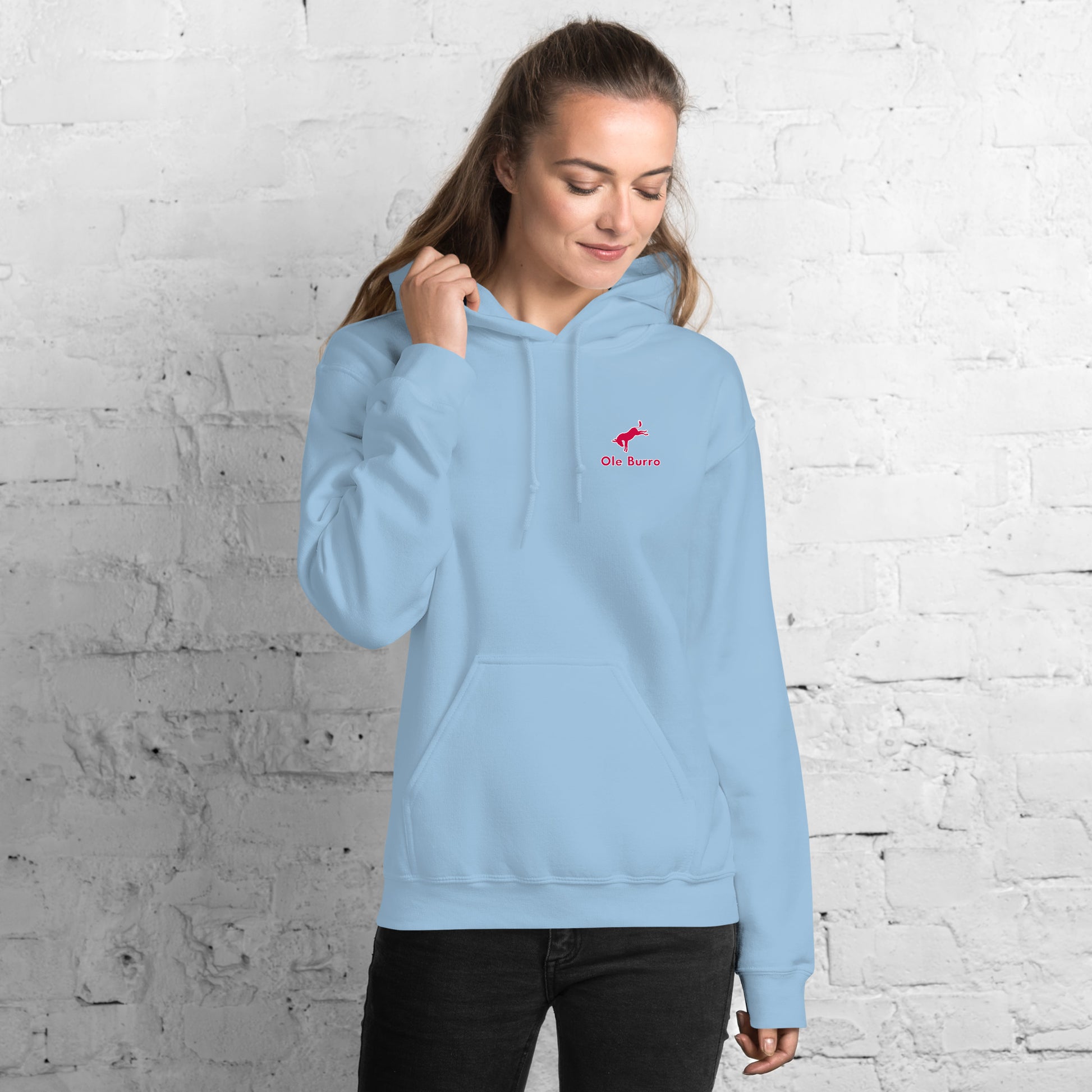Woman wearing a light blue hoodie with a red logo against a white brick wall.